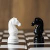 Un caballo blanco y uno negro enfrentados sobre un tablero de ajedrez.