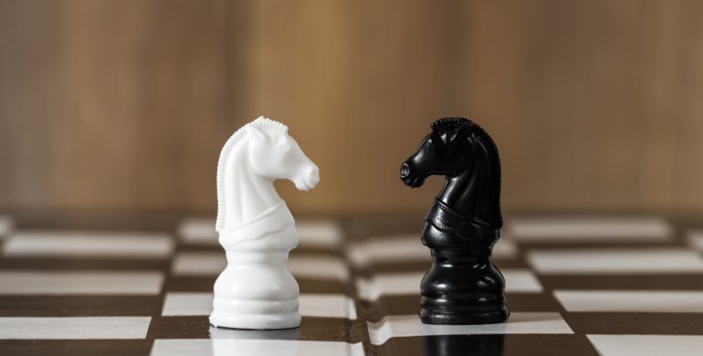 Un caballo blanco y uno negro enfrentados sobre un tablero de ajedrez.